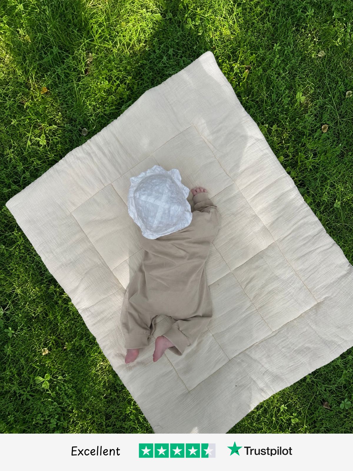 Baby in a beige cotton set lying on a muslin play mat on grass - Little Novice children's clothing, rated Excellent on Trustpilot