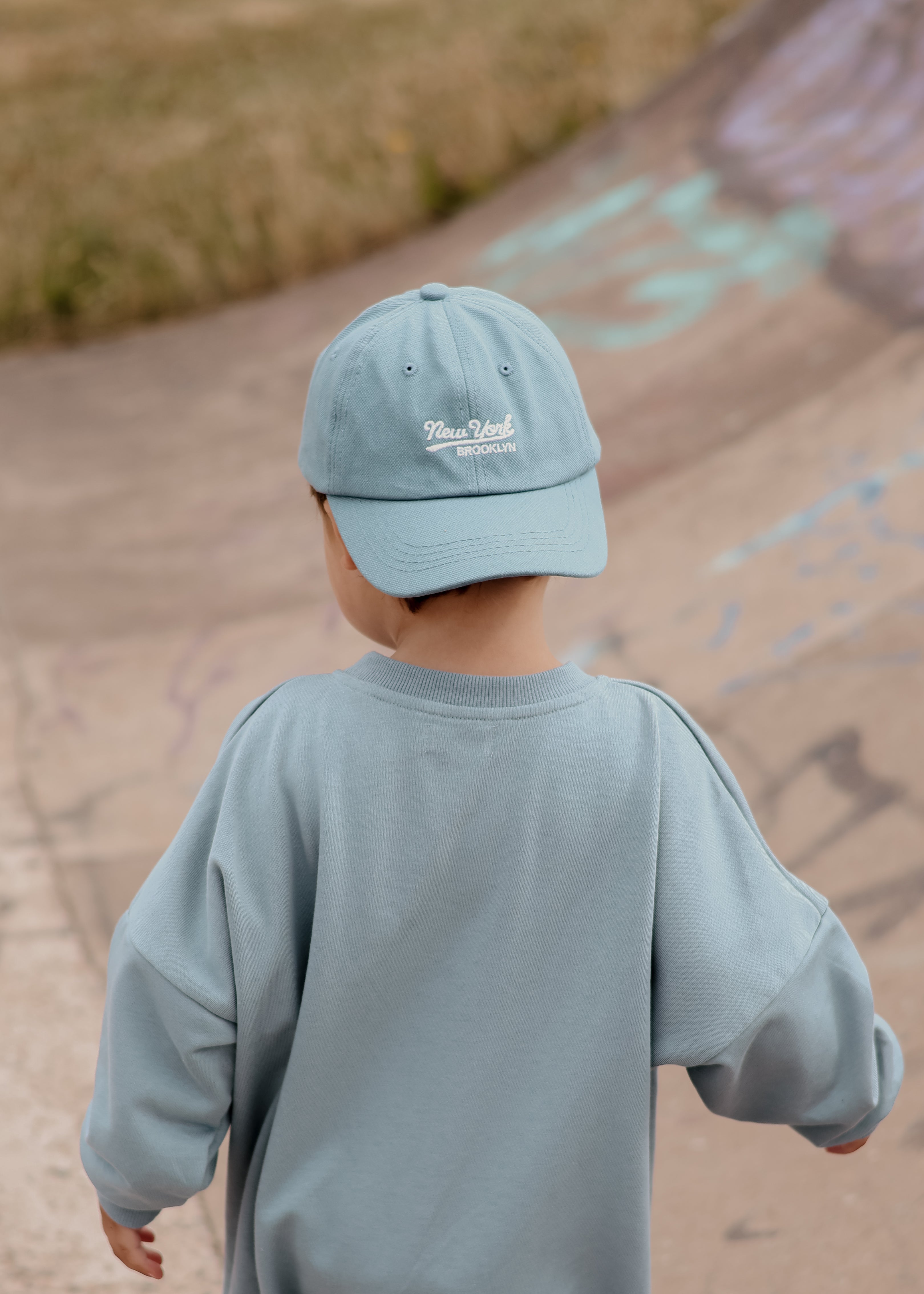 Child wearing a light blue cap and sweatshirt standing on a path with chalk drawings.