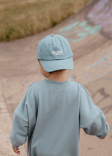 Child wearing a light blue cap and sweatshirt standing on a path with chalk drawings.